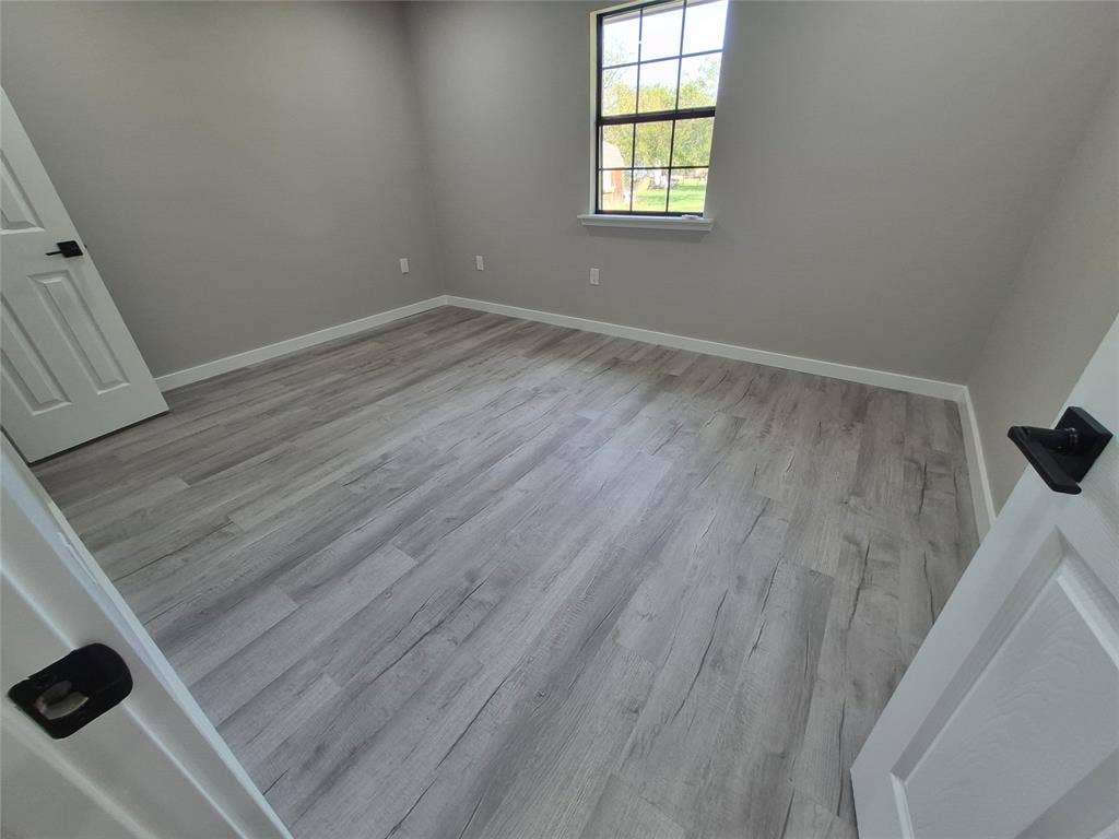 2029 Roberts Drive, Granbury, TX 76048 Interior room featuring wood-finish flooring, neutral wall tones, a grid-pattern window, and white paneled doors with matte black hardware