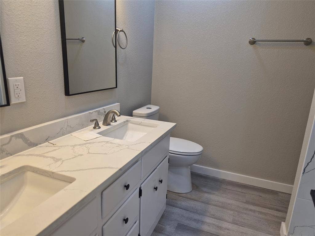 2029 Roberts Drive, Granbury, TX 76048 Double-sink vanity featuring stone-patterned countertops, undermount sinks, matte black hardware, and wood-finish flooring