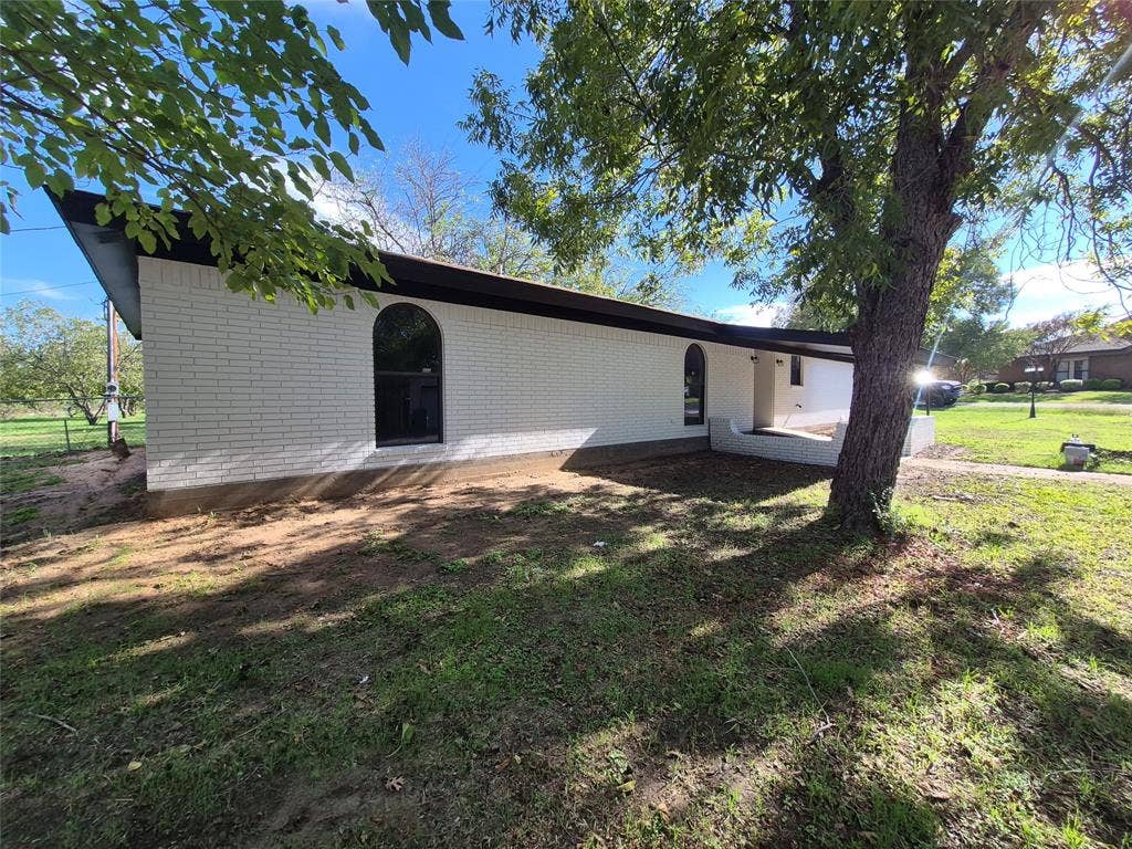 2029 Roberts Drive, Granbury, TX 76048 White painted brick exterior featuring arched window framing, a low-profile roofline, and mature trees on the grounds