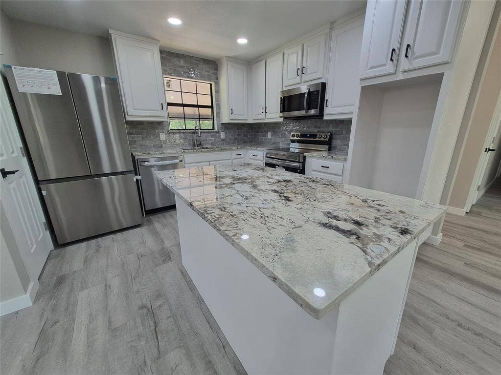 2029 Roberts Drive, Granbury, TX 76048 Kitchen featuring a central island with stone countertop, white shaker-style cabinetry, stainless steel appliances, decorative tile backsplash, and wood-finish flooring