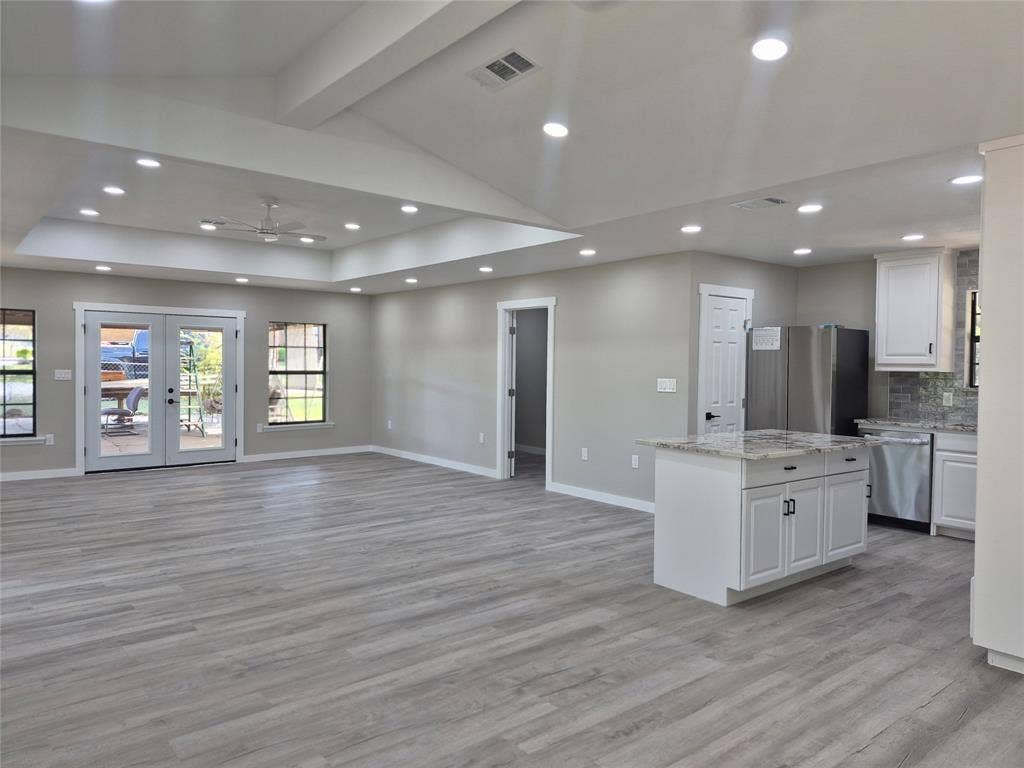 2029 Roberts Drive, Granbury, TX 76048 Open-concept interior featuring a vaulted tray ceiling, recessed lighting, wood-finish flooring, a kitchen island with stone countertops, and French doors