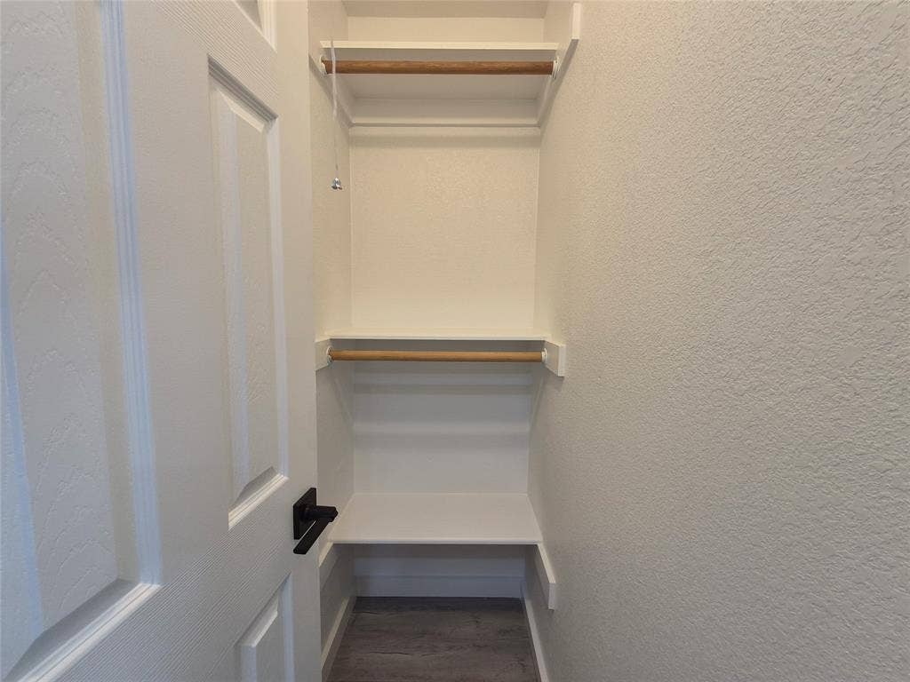 2029 Roberts Drive, Granbury, TX 76048 Storage space featuring dual-level shelving, integrated wood-finish garment rods, and a white six-panel door with matte black hardware