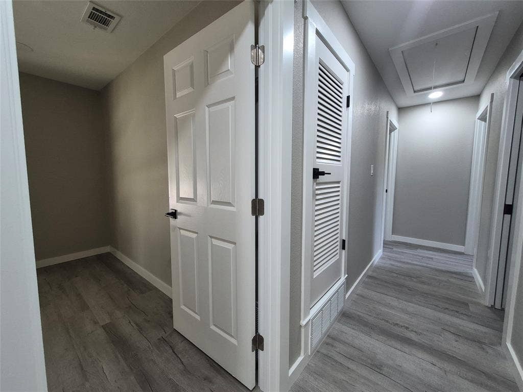 2029 Roberts Drive, Granbury, TX 76048 Hallway featuring wood-finish flooring, six-panel interior doors with matte black hardware, and an integrated louvered door utility closet