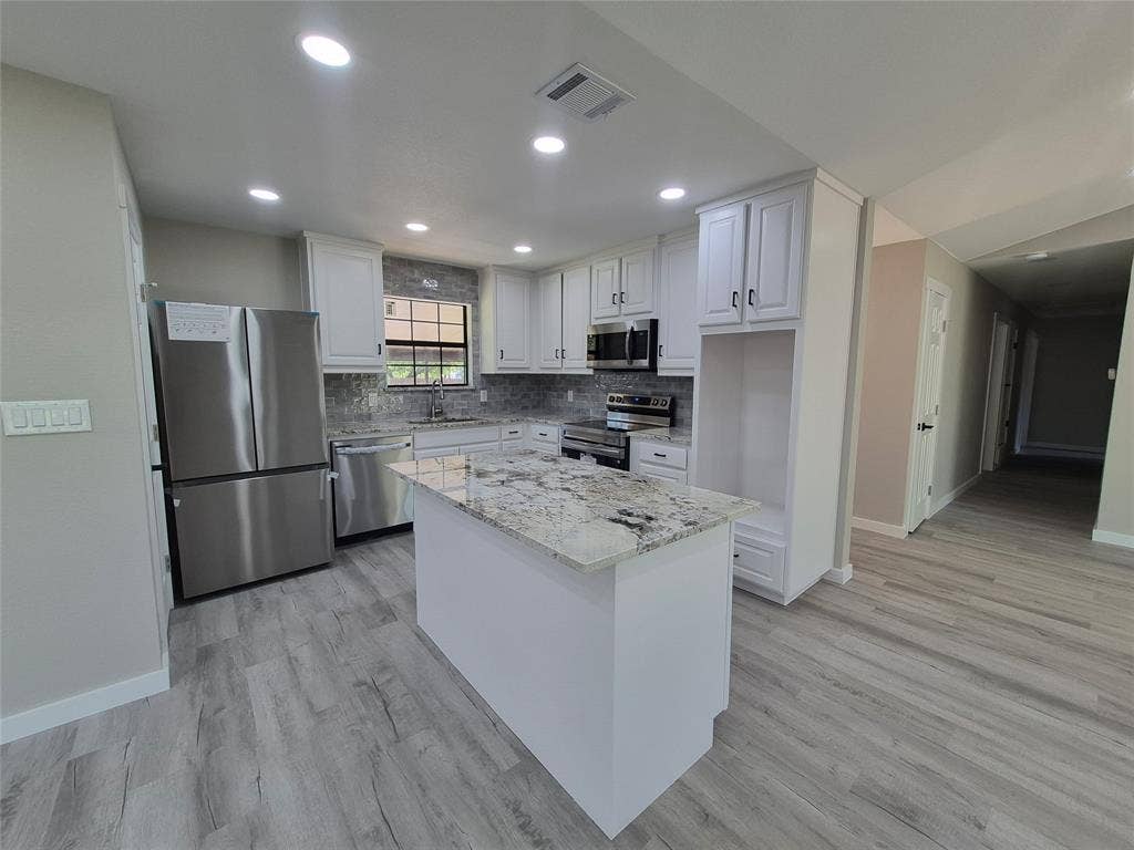 2029 Roberts Drive, Granbury, TX 76048 Kitchen featuring white shaker-style cabinetry, stone-surface countertops, stainless steel appliances, a center island, and wood-finish flooring