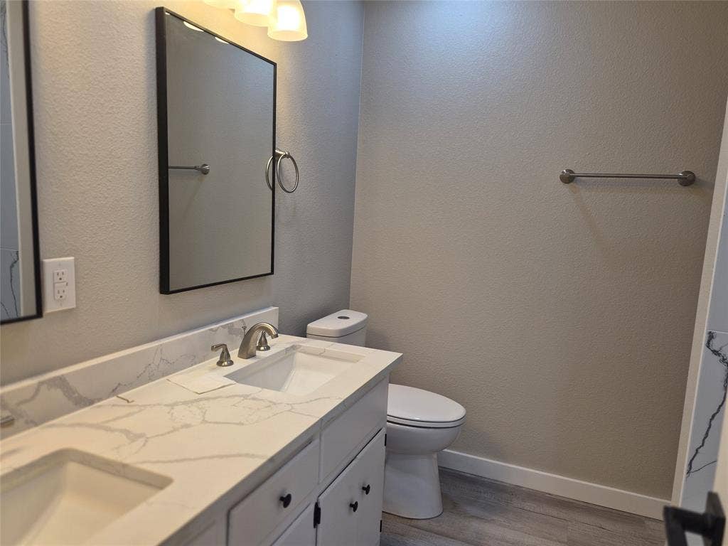 2029 Roberts Drive, Granbury, TX 76048 Double vanity featuring a light-toned stone-finish countertop with integrated dual sinks, sleek black hardware, framed wall mirrors, and wood-finish flooring