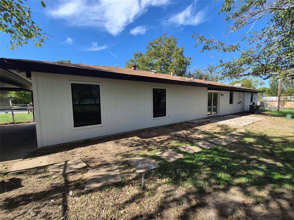 2029 Roberts Drive, Granbury, TX 76048 Single-story exterior featuring light-colored vertical siding, dark window trim, a covered side patio, and square concrete paver stepping stones