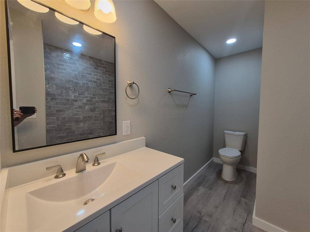 2029 Roberts Drive, Granbury, TX 76048 Vanity with a solid-surface countertop and integrated sink, rectangular mirror with a dark frame, metallic wall-mounted hardware, and wood-finish flooring