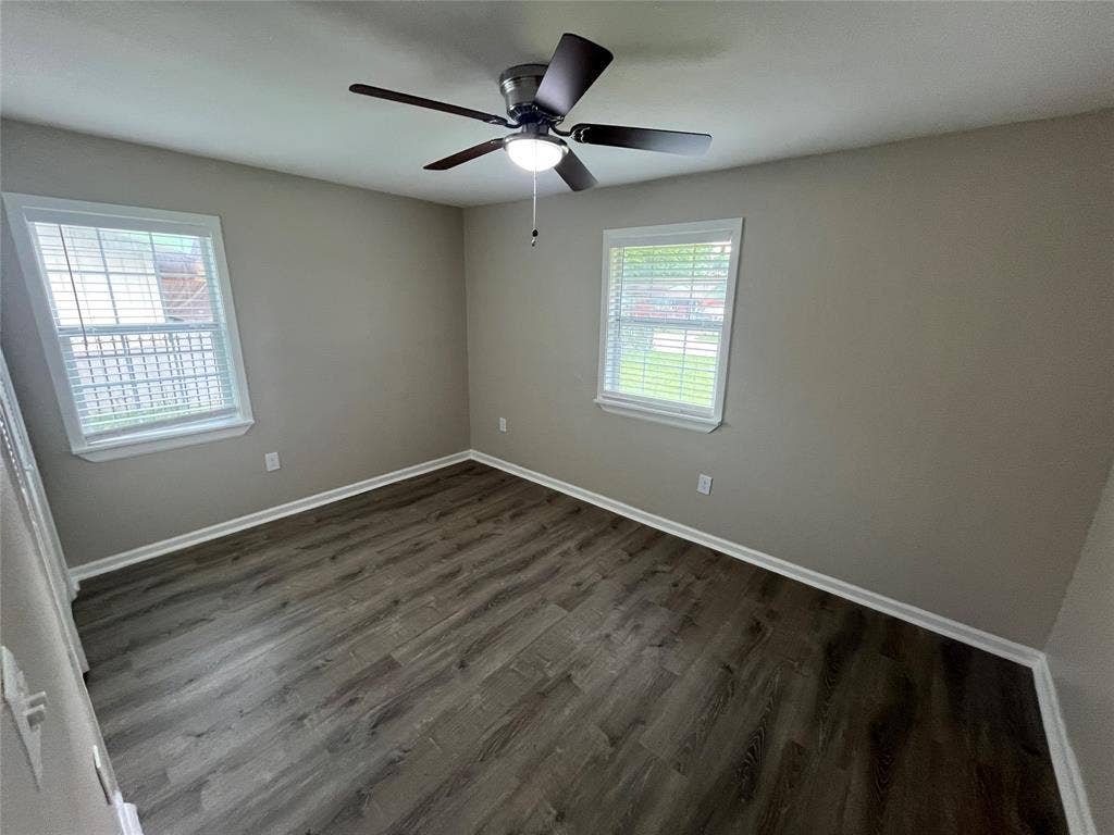 6415 Godfrey Avenue, Dallas, TX 75217 Room featuring neutral-toned walls, wood-finish flooring, two windows with horizontal blinds, and a central ceiling fan with an integrated light fixture