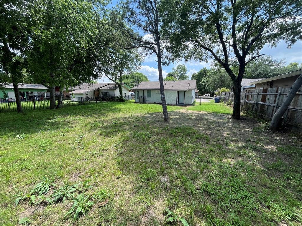 6415 Godfrey Avenue, Dallas, TX 75217 Expansive backyard featuring mature trees, wood fence perimeter, and metal rod fencing