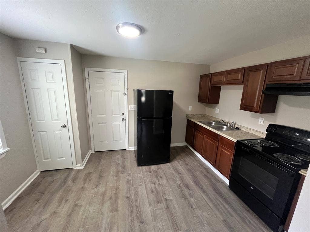 6415 Godfrey Avenue, Dallas, TX 75217 Kitchen featuring dark wood-finish cabinetry, solid-surface countertops, black finish appliances, and wood-finish flooring