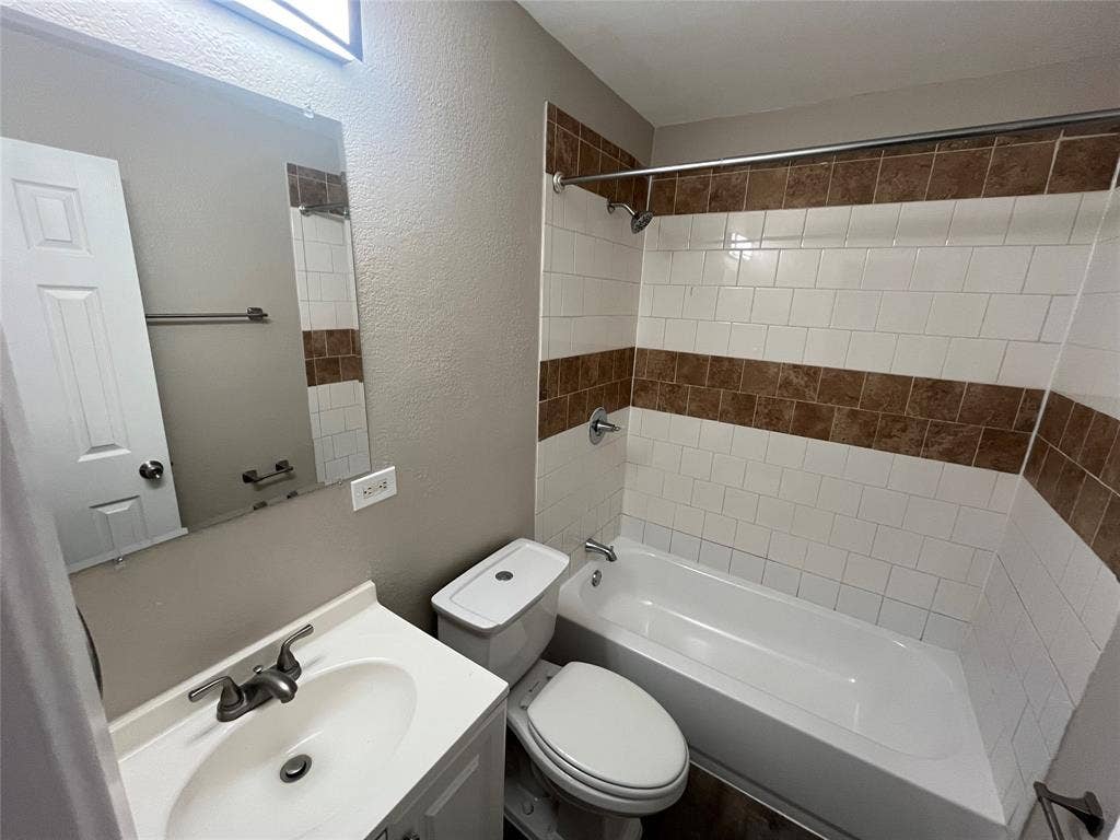 6415 Godfrey Avenue, Dallas, TX 75217 Bathroom featuring a white vanity with an integrated sink, polished chrome faucet, rectangular wall-mounted mirror, and a tub-shower combination with decorative tile inlay