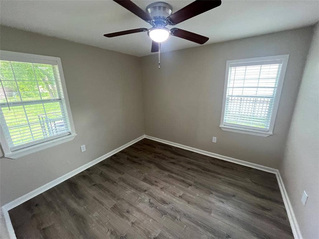 6415 Godfrey Avenue, Dallas, TX 75217 Neutral-toned interior space featuring wood-finish flooring, dual windows with horizontal blinds, and a central ceiling fan with integrated lighting