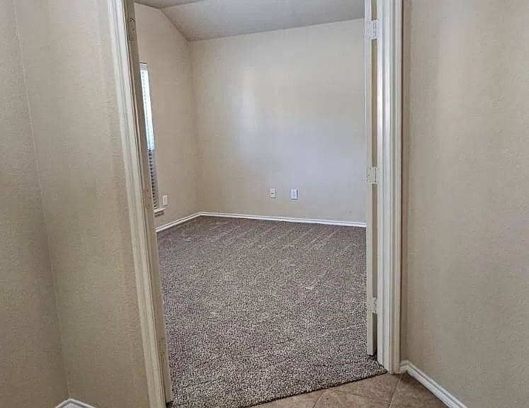 1000 Buffalo Creek Drive, McKinney, TX 75072 Neutral-toned interior space featuring textured wall-to-wall carpeting, vaulted ceiling, dual-swing doors, and a window with fitted blinds