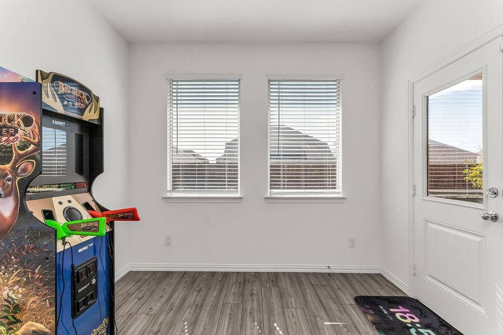 Neutral-toned room featuring vinyl flooring, dual windows with horizontal blinds, and a paneled exterior door with a glass insert