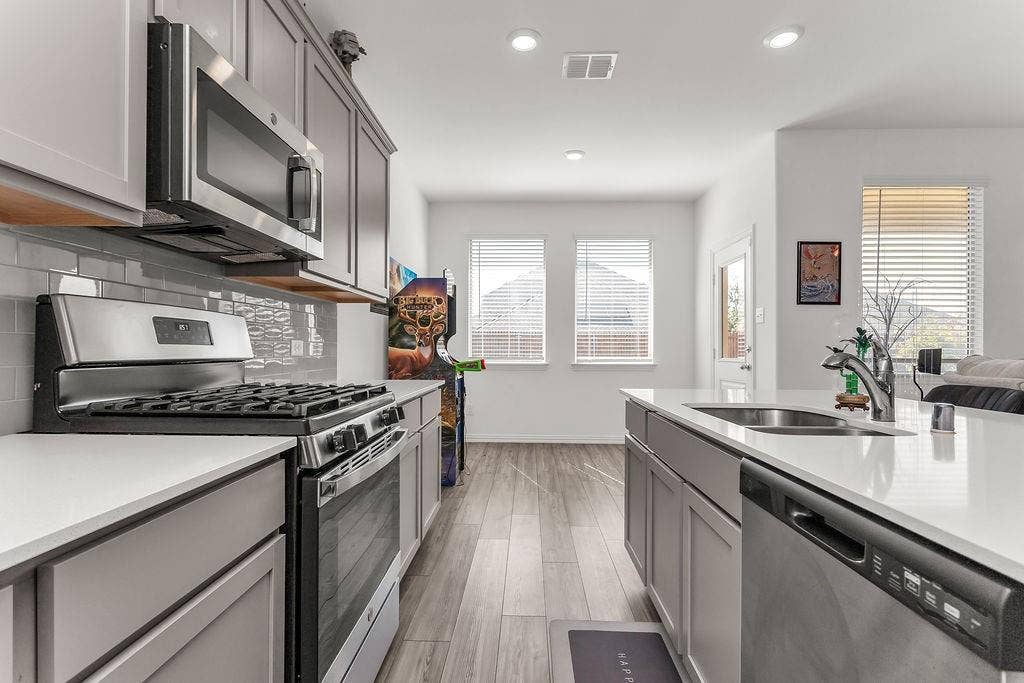Kitchen featuring grey shaker-style cabinetry, quartz countertops, stainless steel appliances, grey subway tile backsplash, and vinyl flooring