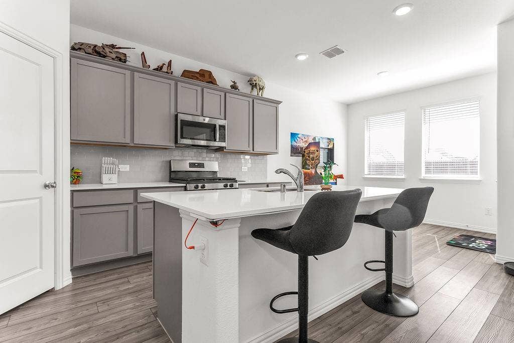 Kitchen featuring grey shaker-style cabinetry, white countertops, a central island with an integrated sink, stainless steel appliances, and vinyl flooring