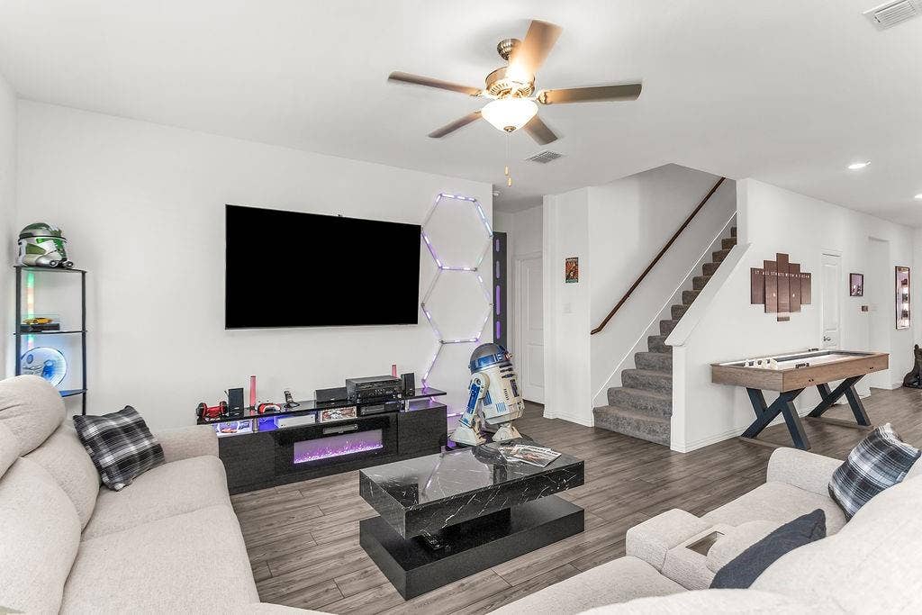 Open-concept room featuring vinyl flooring, a ceiling fan with integrated lighting, and a staircase with a wooden handrail