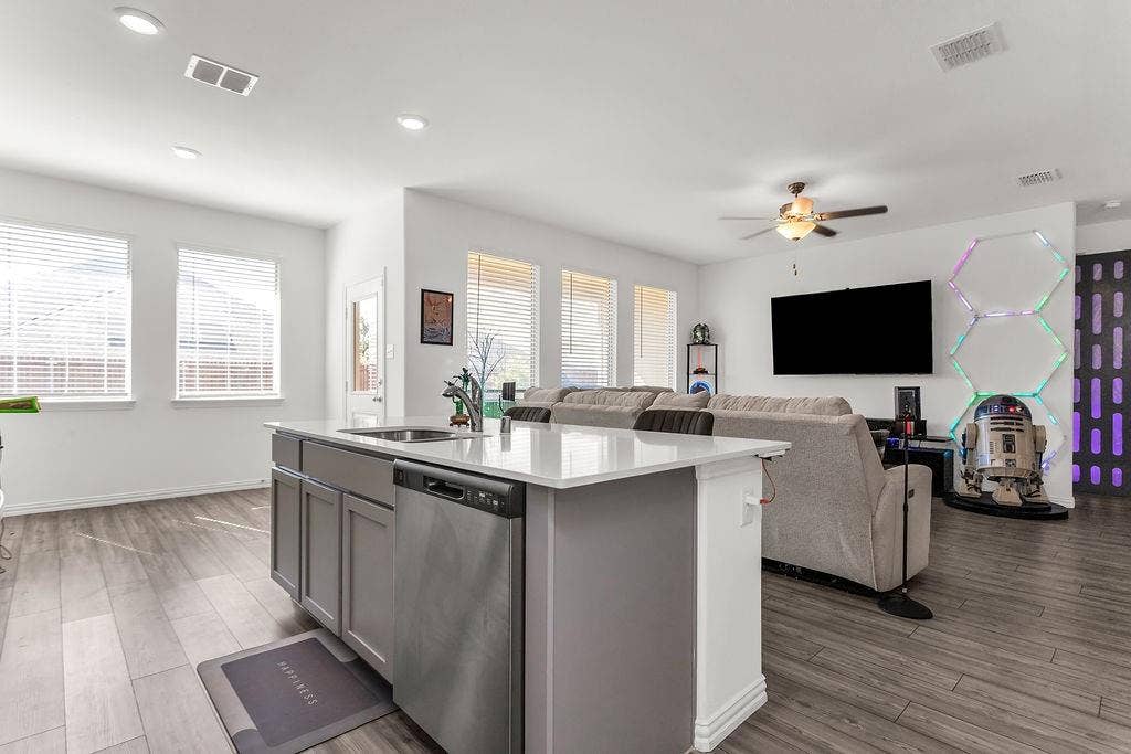 Kitchen island featuring a quartz countertop, stainless steel dishwasher, and undermount sink, complemented by vinyl flooring and recessed lighting