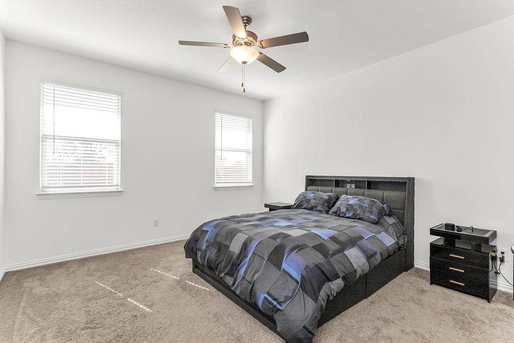 Neutral-toned interior space featuring neutral carpeting, two windows with horizontal blinds, and a central ceiling fan with integrated lighting