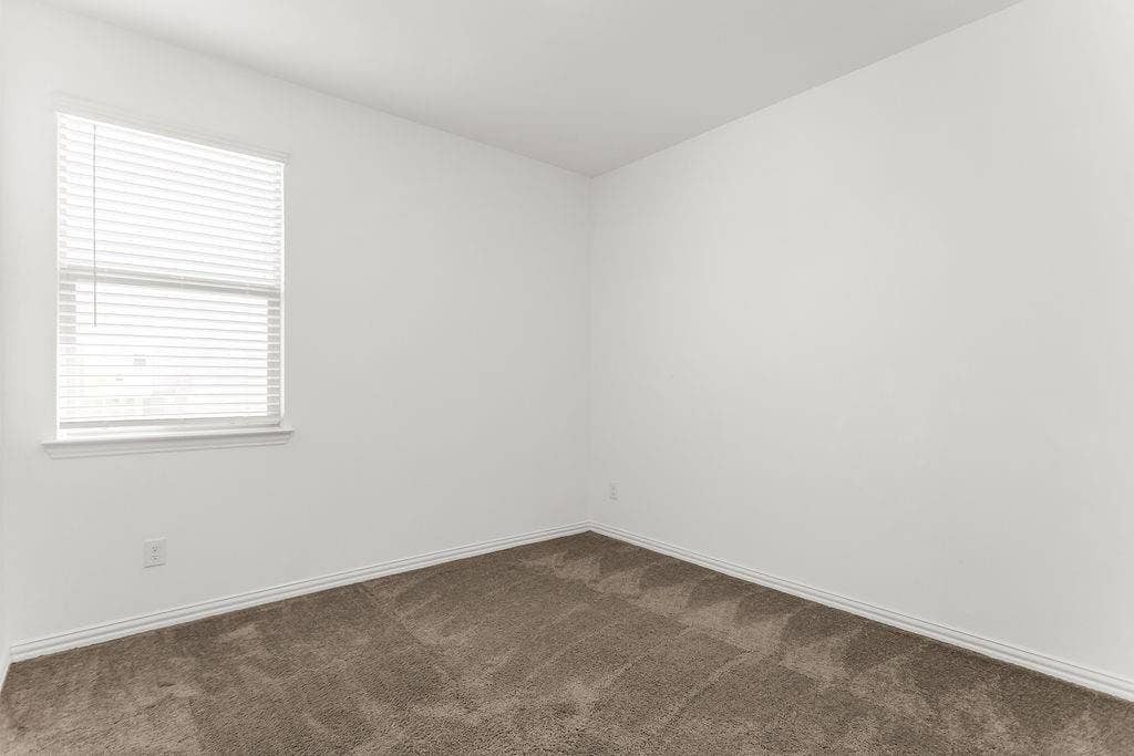 Neutral interior space featuring crisp white walls, neutral-toned wall-to-wall carpeting, and a window with horizontal blinds