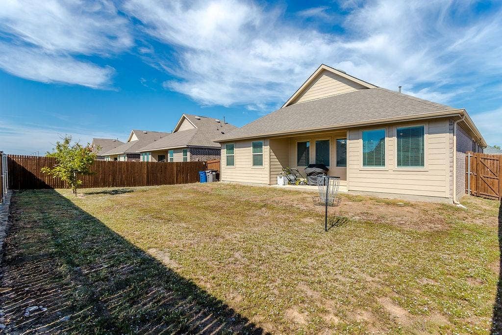 Rear exterior featuring light-toned horizontal siding, a gabled roofline, multiple windows, and a fenced backyard