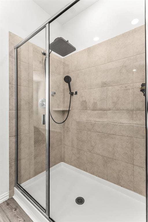 Walk-in shower featuring glass paneling, floor-to-ceiling tile surround, square rainfall shower head, handheld sprayer, and integrated corner shelving