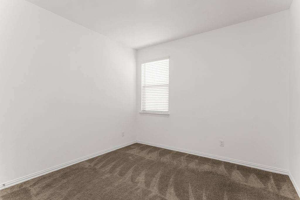 Neutral-toned wall finish, wall-to-wall carpeting, and a single-pane window with horizontal blinds