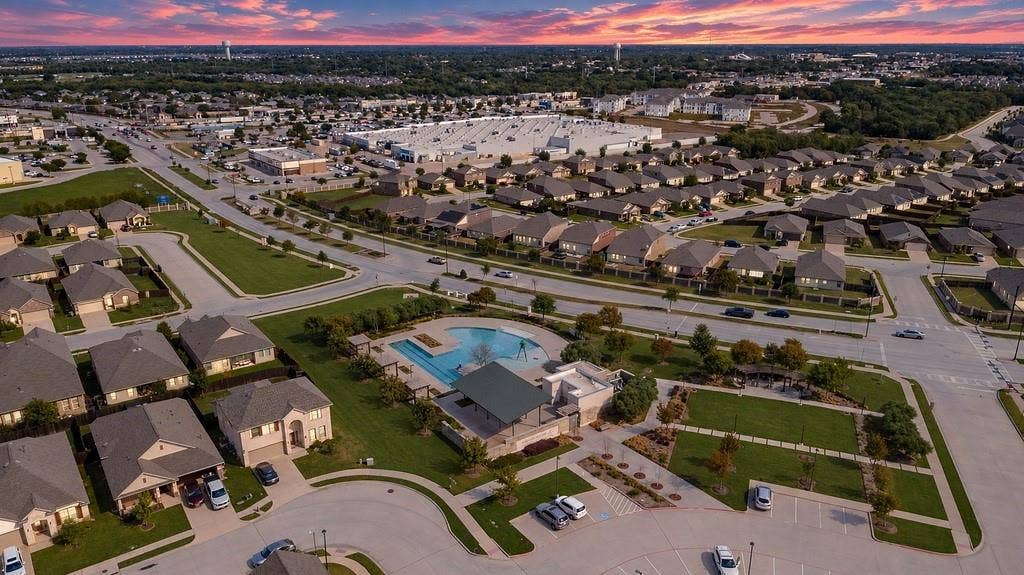Aerial perspective featuring a community swimming pool, covered pavilion, manicured green space, paved parking area, and sunset horizon