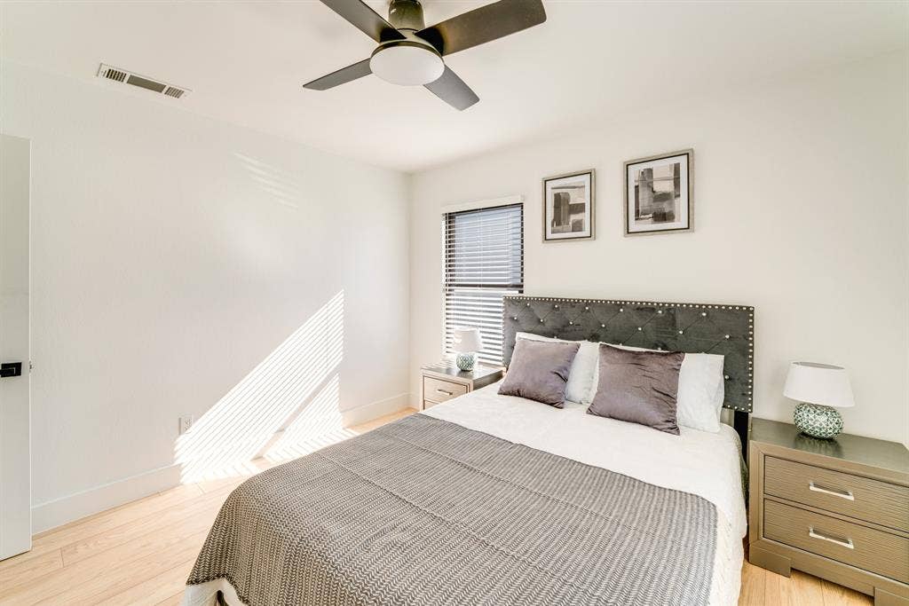 Wood-finish flooring, neutral wall tones, multi-blade ceiling fan with integrated lighting, and window blinds
