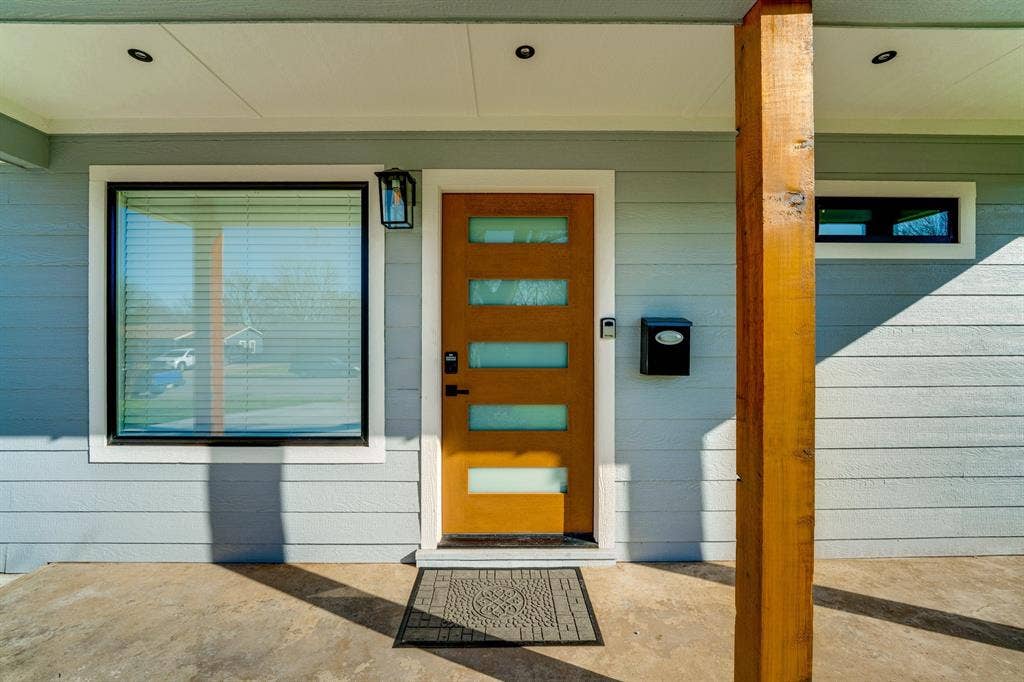 Covered entryway featuring horizontal siding, a natural wood-finish front door with horizontal glass inserts, recessed lighting, and an exposed wooden support post