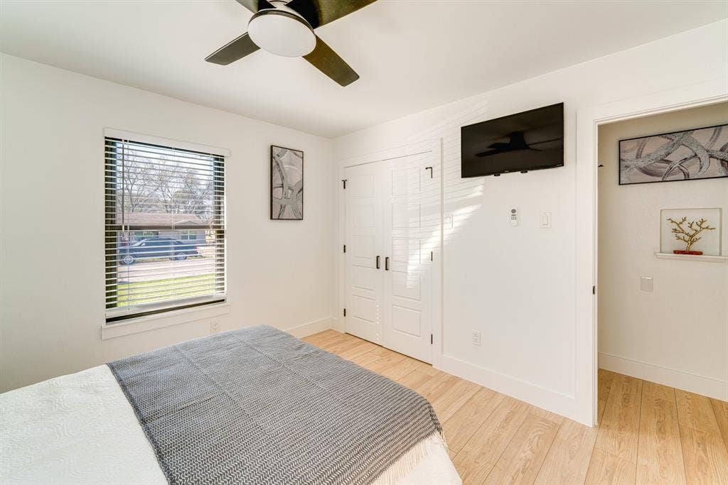 Light-filled room featuring wood-finish flooring, a ceiling fan with integrated lighting, a single-hung window with horizontal blinds, and paneled double closet doors