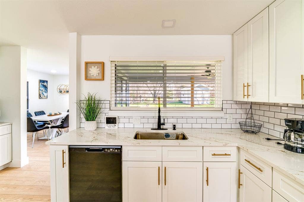 Kitchen featuring white Shaker-style cabinetry, gold-tone hardware, white subway tile backsplash, stone-finish countertops, and a single-basin undermount sink with a matte black faucet