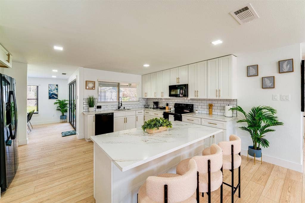Kitchen featuring white cabinetry with gold-toned hardware, a quartz-surfaced island, subway tile backsplash, and light-toned wood-finish flooring