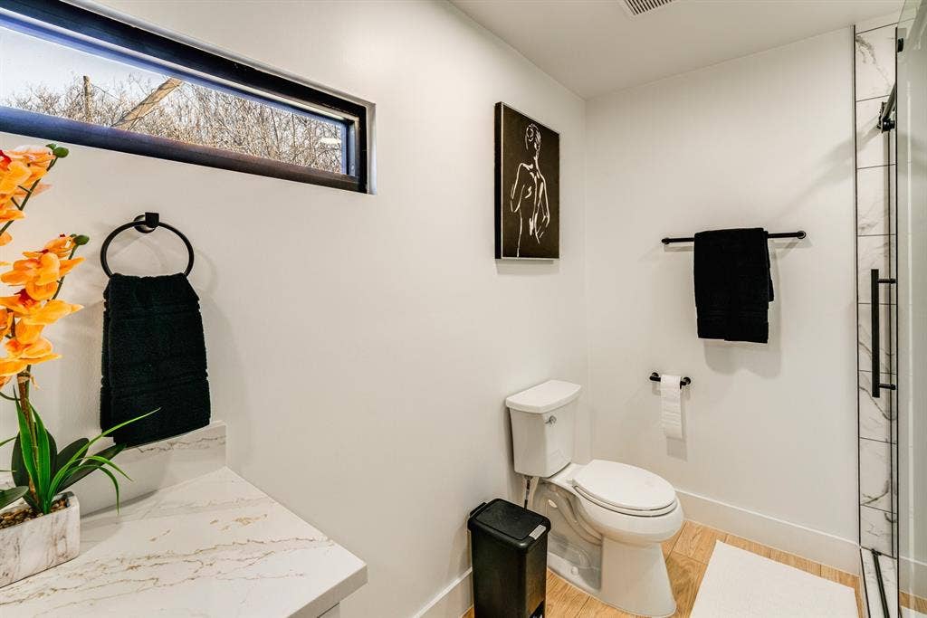 Bathroom featuring a horizontal clerestory window, stone-finish vanity countertop, wood-finish flooring, and a walk-in shower with tiled surround