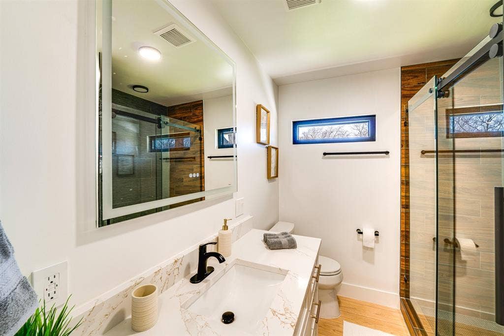 Bathroom featuring a vanity with a white countertop, matte black faucet, illuminated mirror, walk-in shower with a sliding glass door, and wood-finish flooring