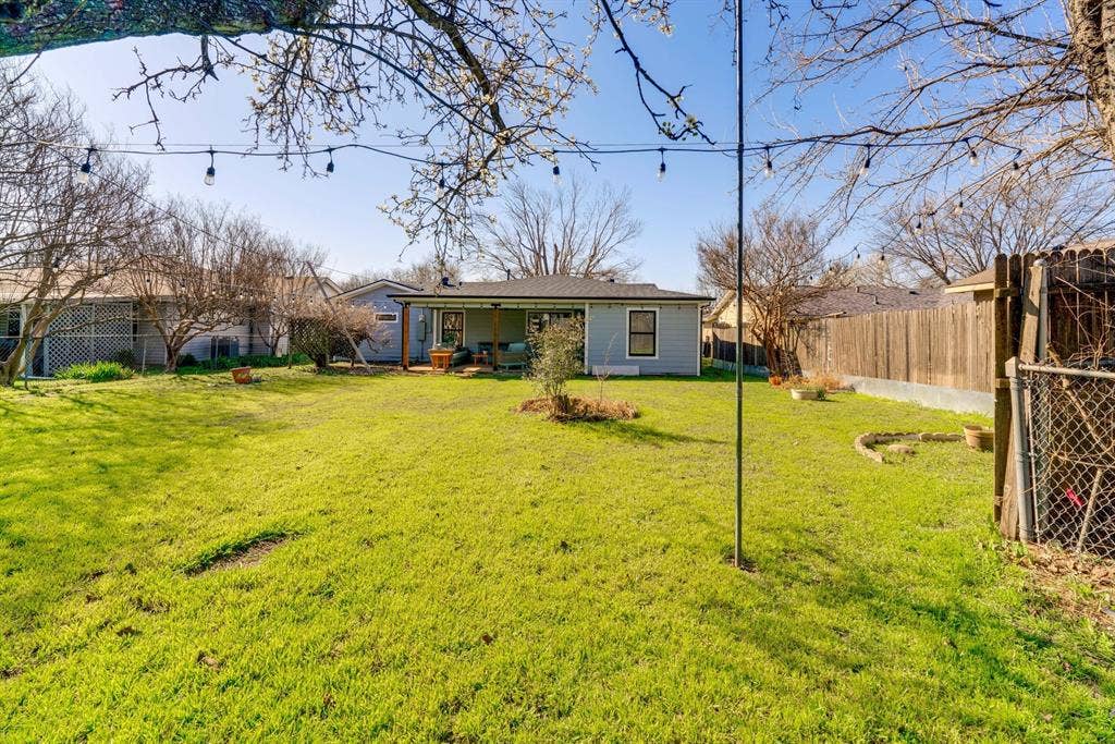 Expansive backyard featuring a lawn, wood fencing, mature trees, and a covered rear patio