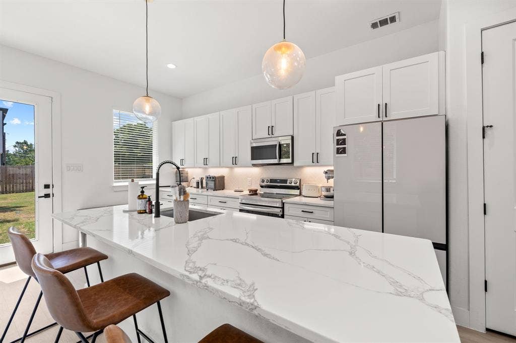 2502 Elsie Faye Heggins Street, Dallas, TX 75215 Kitchen featuring white cabinetry, quartz countertops with veining, stainless steel appliances, matte black hardware, and pendant lighting