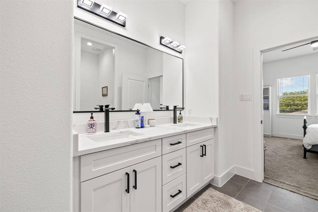 2502 Elsie Faye Heggins Street, Dallas, TX 75215 Double vanity featuring white cabinetry, stone-finish countertops with integrated sinks, matte black hardware, and dual wall-mounted light fixtures
