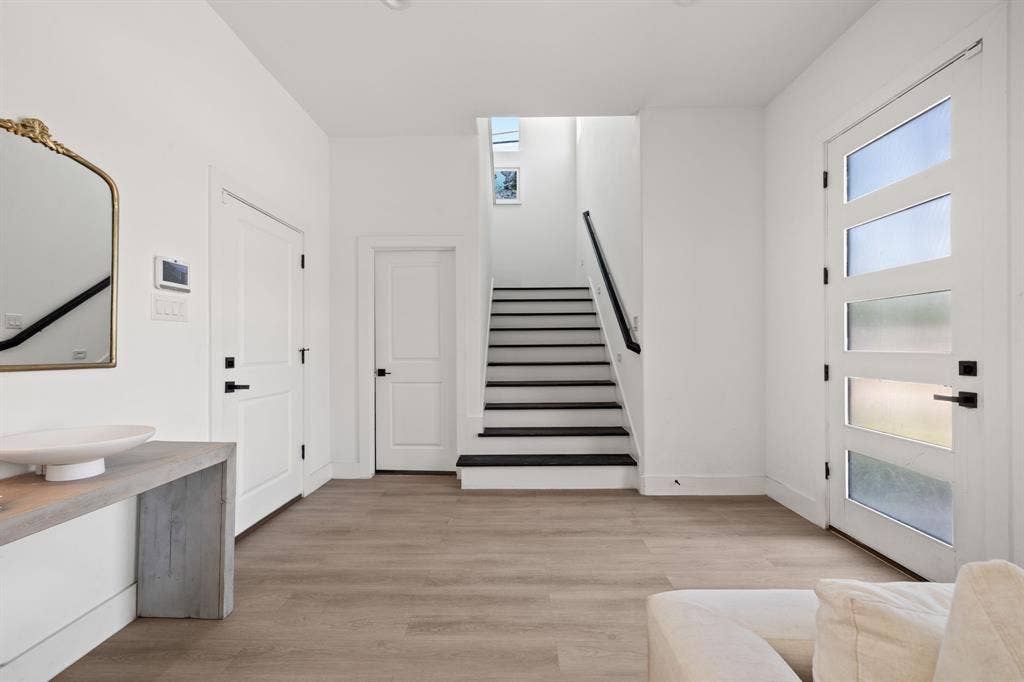2502 Elsie Faye Heggins Street, Dallas, TX 75215 Entryway featuring wood-finish flooring, a contemporary door with horizontal glass panels, a floating vanity with a vessel sink, and a staircase with contrasting dark treads
