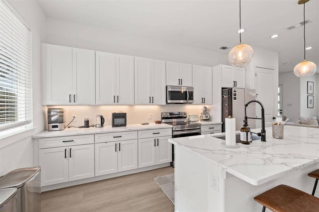 2502 Elsie Faye Heggins Street, Dallas, TX 75215 Kitchen featuring white shaker-style cabinetry, white countertops with grey veining, a central island with a matte black faucet, stainless steel appliances, and wood-finish flooring