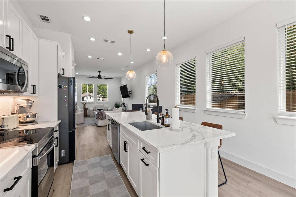 2502 Elsie Faye Heggins Street, Dallas, TX 75215 Kitchen featuring a central island with a stone-finish countertop, white cabinetry with matte black hardware, stainless steel appliances, wood-finish flooring, and pendant lighting