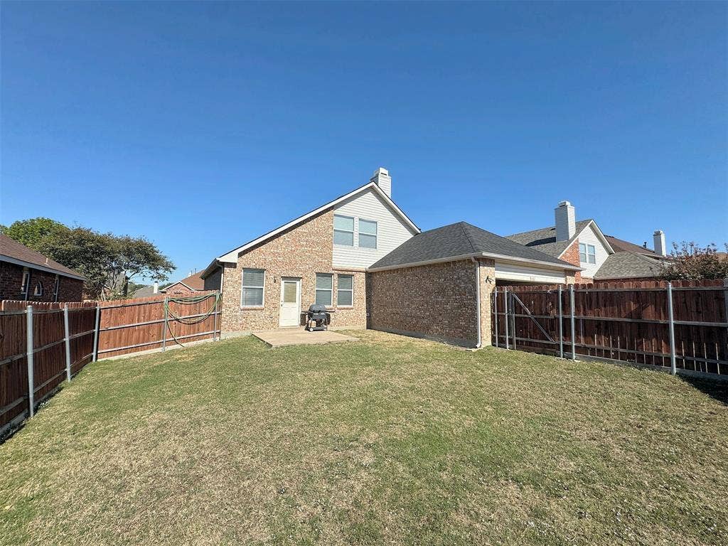 4102 Maidstone Drive, Garland, TX 75043 Alternate backyard view showing the rear elevation, lawn, concrete patio, and fenced outdoor space.