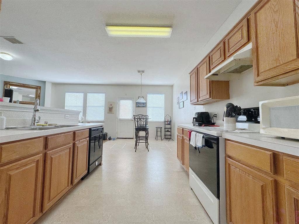4102 Maidstone Drive, Garland, TX 75043 Kitchen view highlighting wood cabinetry, light countertops, cooking appliances, and a central walkway toward the windowed dining area.