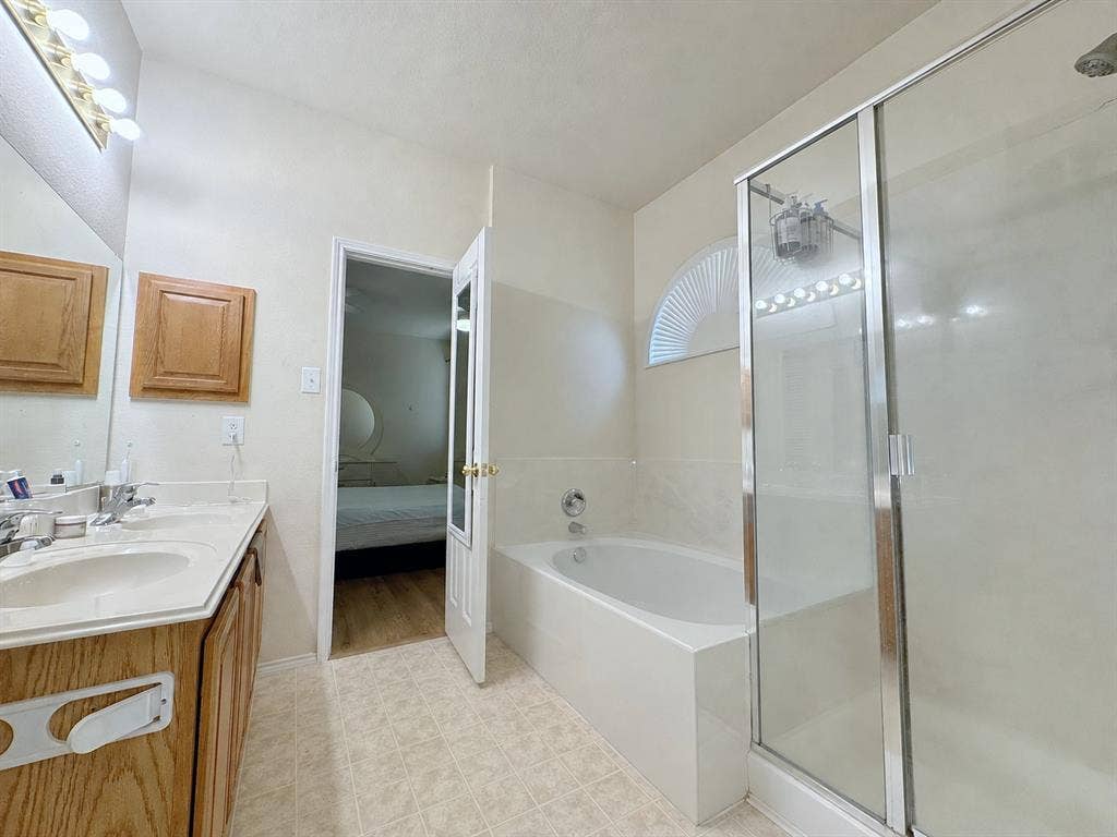 4102 Maidstone Drive, Garland, TX 75043 Bathroom view showing the glass-enclosed shower, adjacent bathtub, light-colored tile, and part of the vanity area.