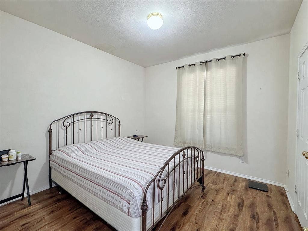 4102 Maidstone Drive, Garland, TX 75043 Bedroom with a metal bed frame, wood-look flooring, light-colored walls, and a curtained window.