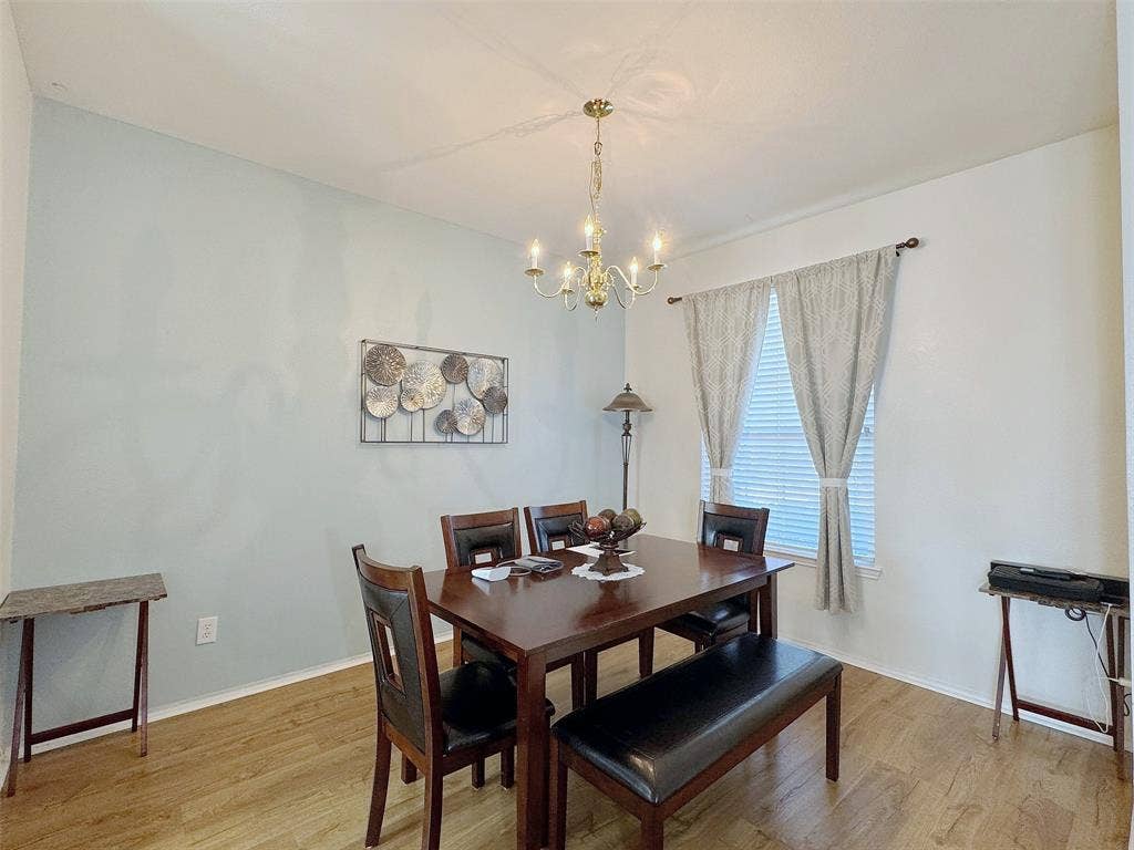 4102 Maidstone Drive, Garland, TX 75043 Dining area with a chandelier, window treatments, wood-look flooring, and space for a dining table and additional furnishings.