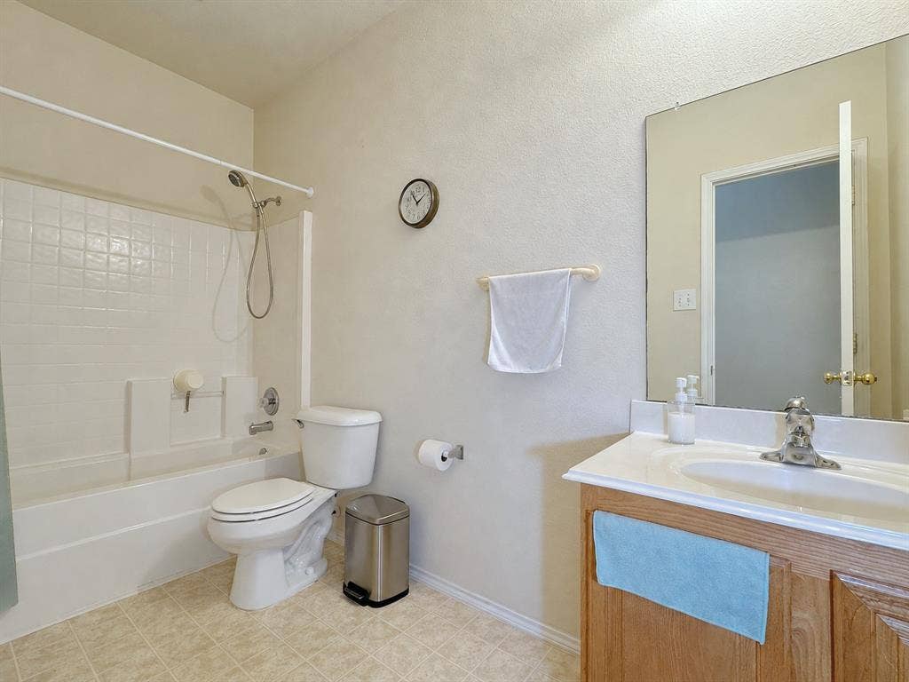 4102 Maidstone Drive, Garland, TX 75043 Bathroom with a tub-and-shower combination, toilet, wood vanity, light countertop, and wall mirror.
