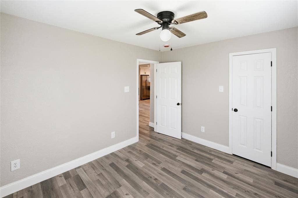 Room featuring wood-finish flooring, a ceiling fan with integrated lighting, neutral wall paint, and two six-panel interior doors