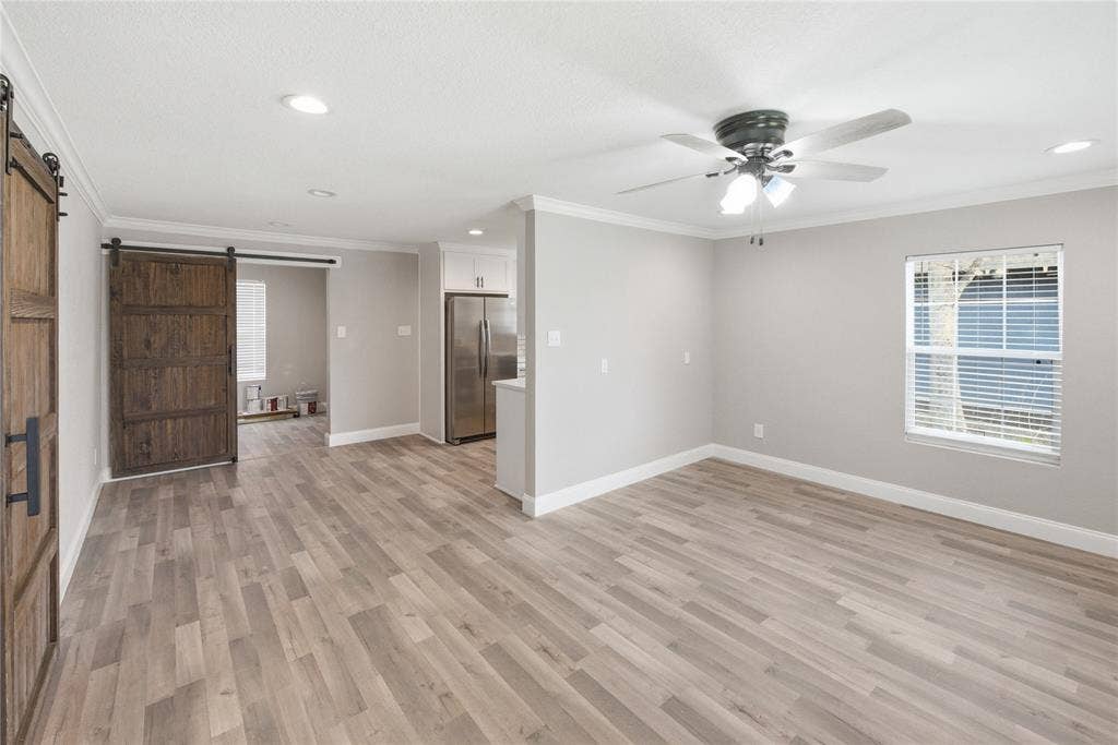 Wood-finish flooring, sliding barn door with dark hardware, recessed lighting, ceiling fan with light kit, and stainless steel refrigerator