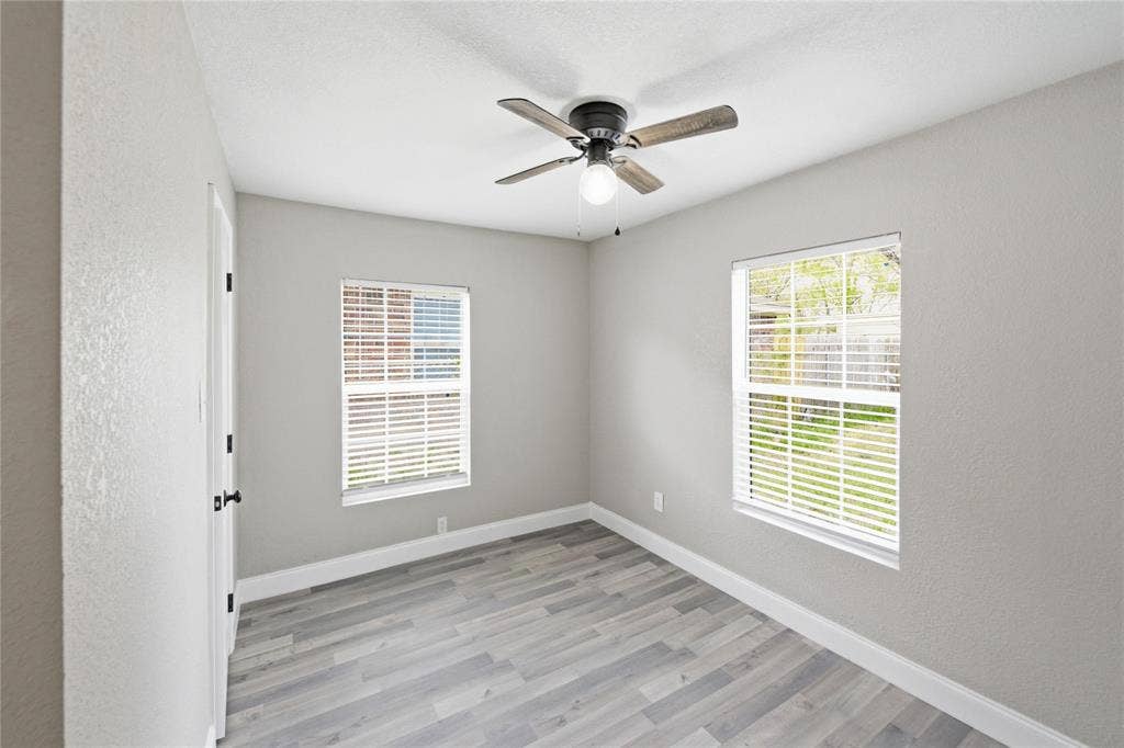Neutral-toned interior featuring wood-finish flooring, dual windows with fitted blinds, and a central ceiling fan